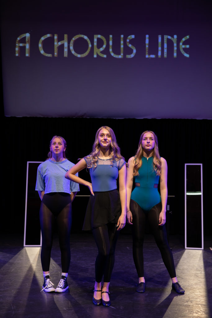 Photo of 3 girls in front of "A Chorus Line" projection