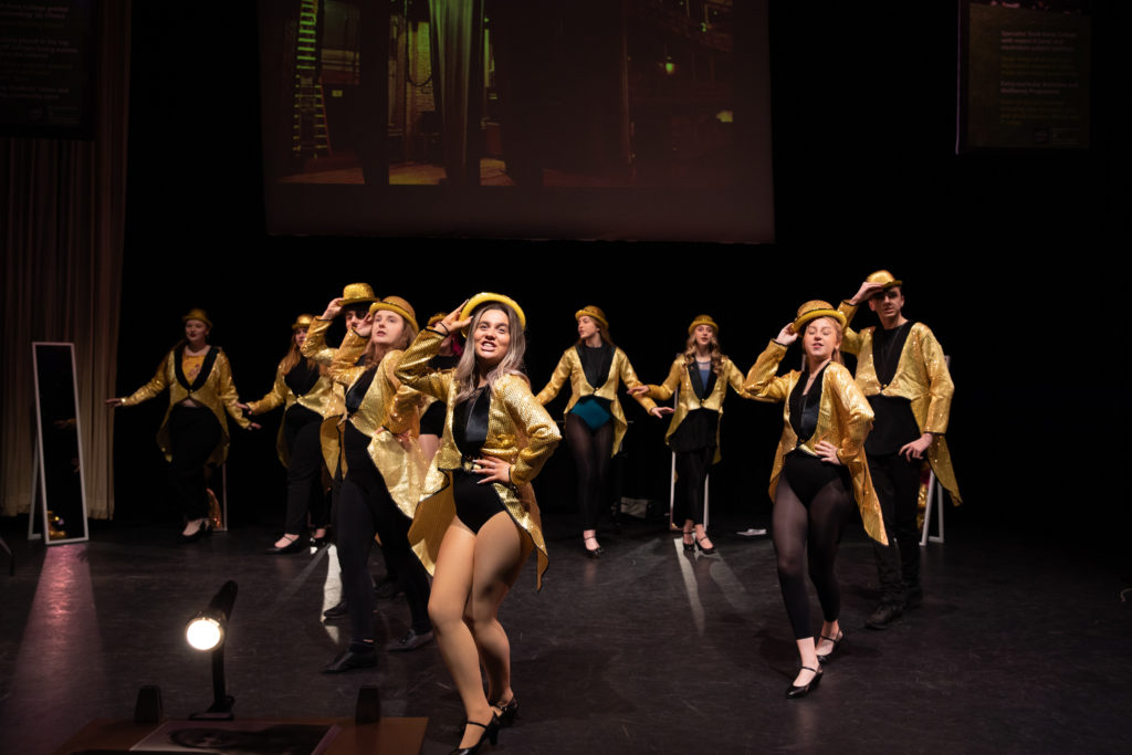Group of students in gold costumes dancing and singing in the "A Chorus Line" performance