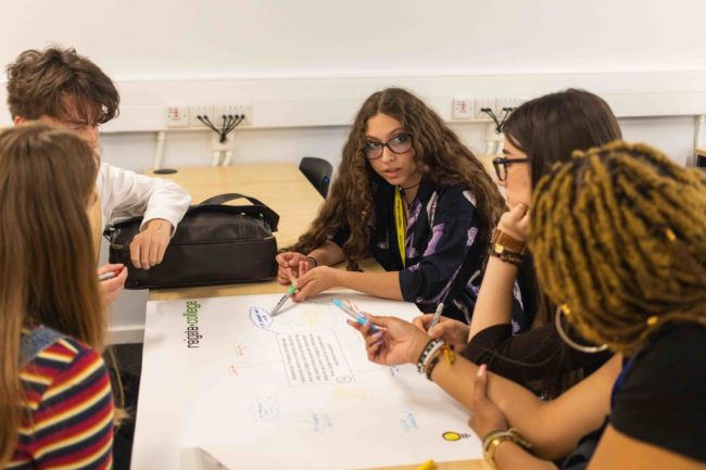Student around a table writing ideas around mental health in young children