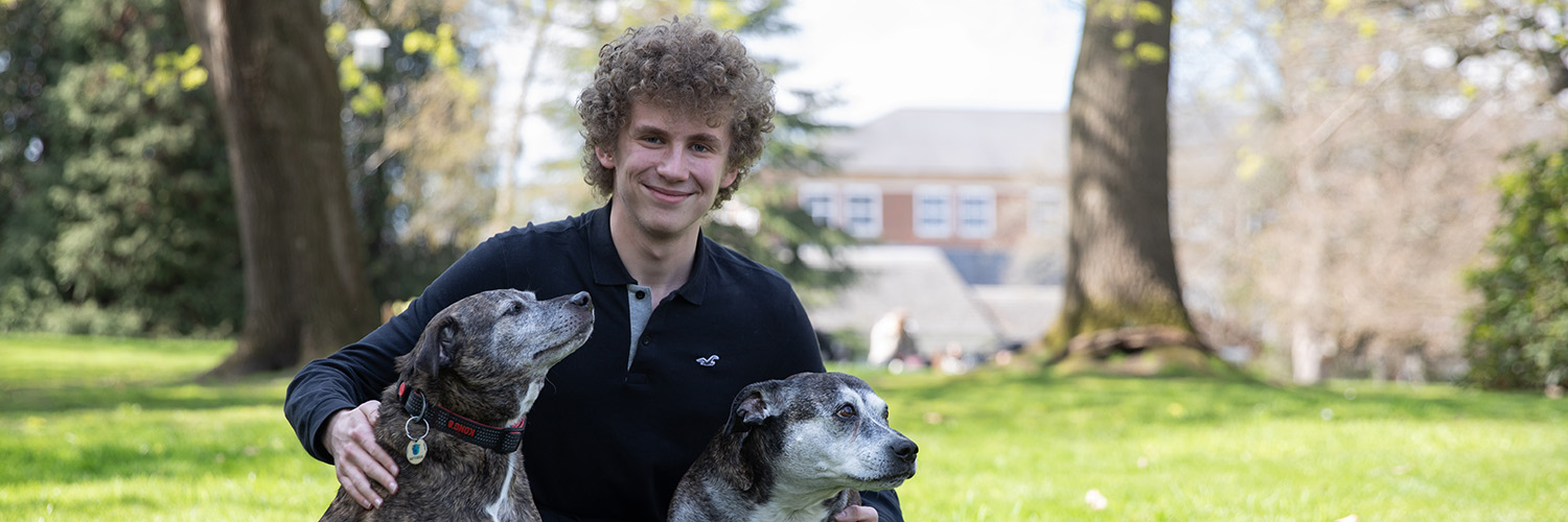 Student sitting on grass with two dogs