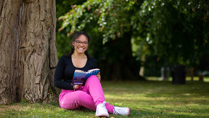 Student sitting on the grass reading a book