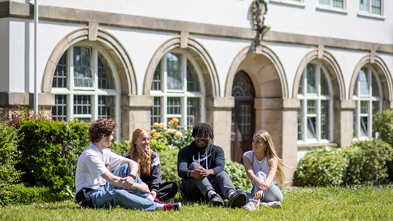 Students sitting on grass outside Reigate College building