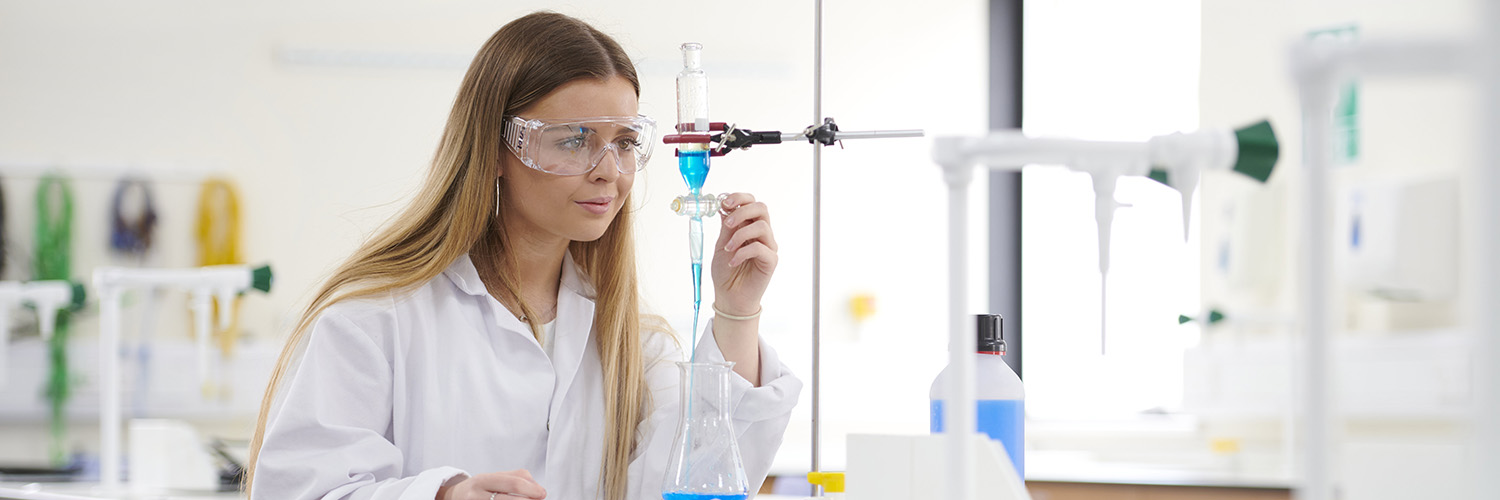 Student wearing a white coat and protective eye wear working in a science laboratory