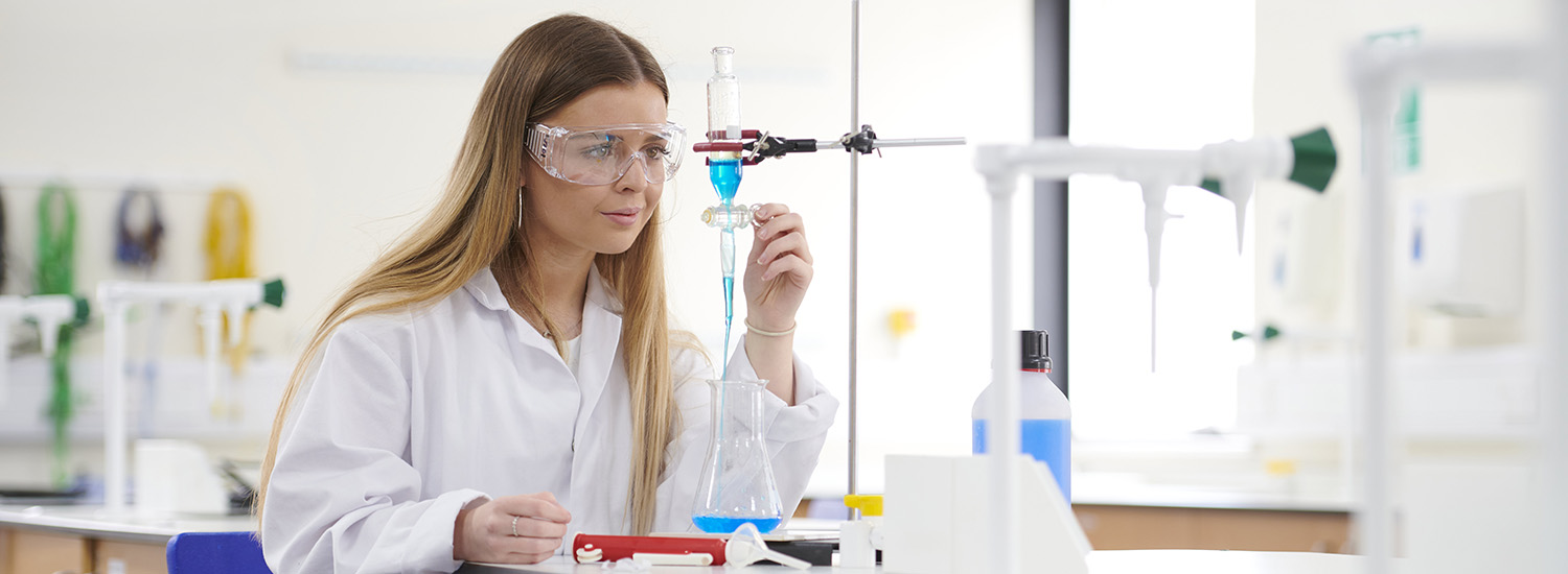 Student wearing a white coat and protective eye wear working in a science laboratory