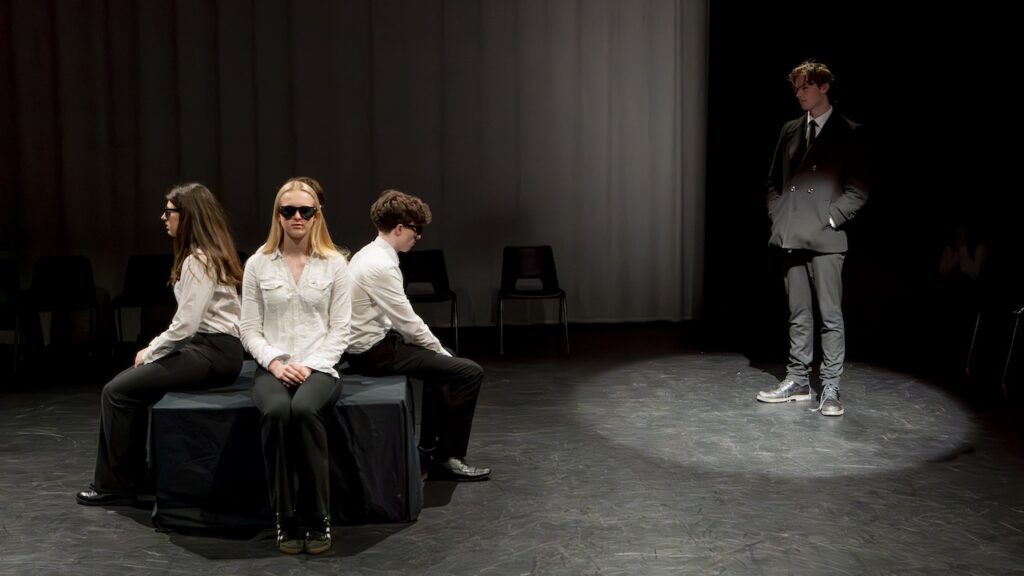 Students on stage performing Antigone in modern costumes