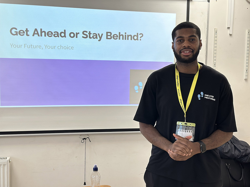 Guest speaker in front of his presentation with the title "Get Ahead or Stay Behind" on the screen.