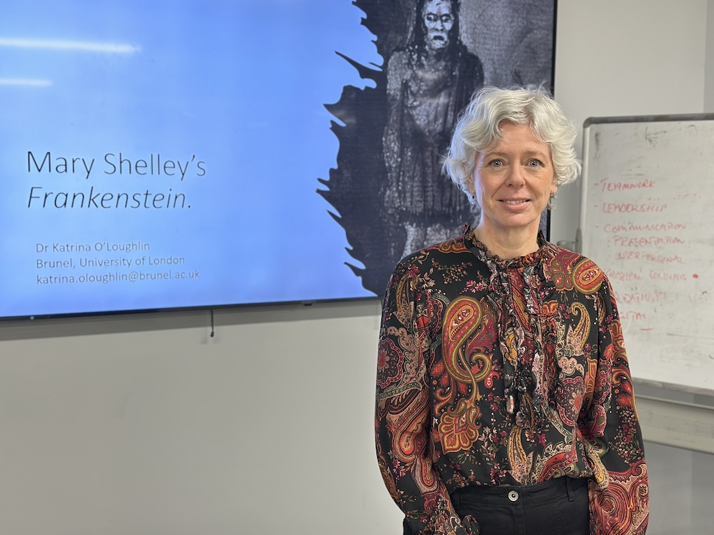 Dr Katrina O'Loughlin standing in front of a screen displaying her presentation about Mary Shelley's Frankenstein